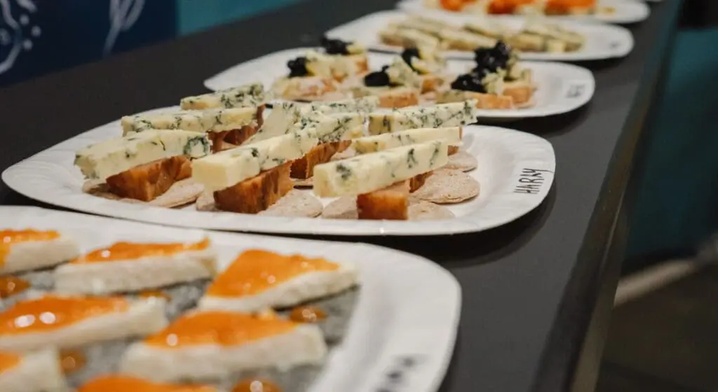 Close up of four white plates with crackers loaded with different cheeses and accompaniments