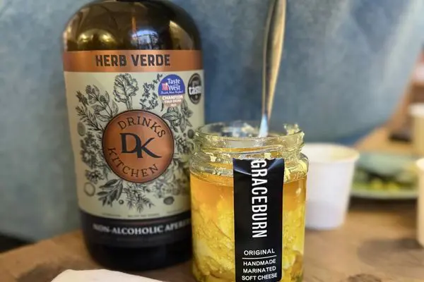 A bottle of Herb Verde non-alcoholic aperitif with a jar of Graceburn "feta"- style cheese and spoon.
