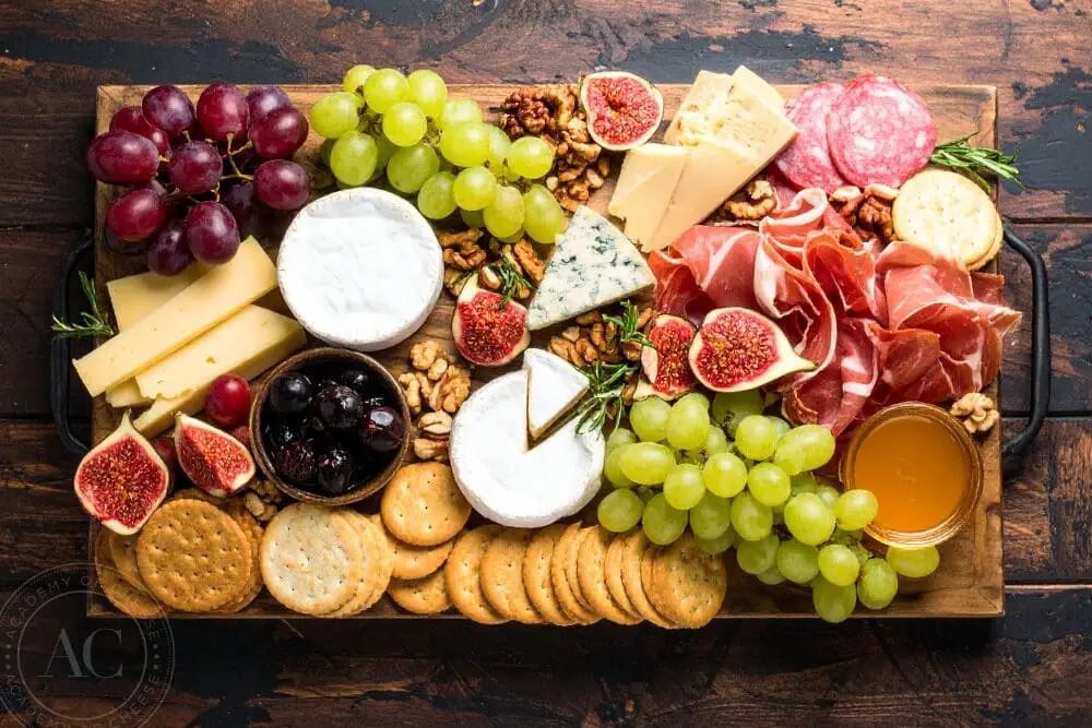 A wooden board with a selection of cheeses, crackers, fruit, nuts and charcuterie meats.