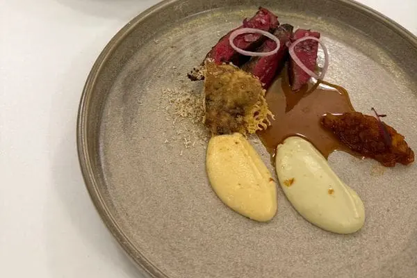 A grey plate with some meat, gravy and cheese puree