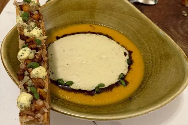 A bowl of butternut squash and stilton soup with a sourdough breadstick resting on the lip