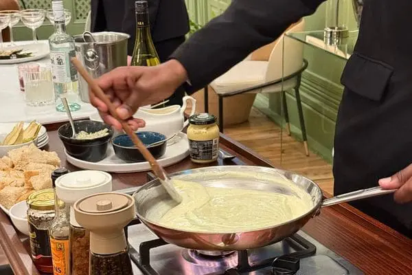 A front-of-house team member stirring fondue in a copper pan over a flame with pepper, worcester sauce and other accompaniments