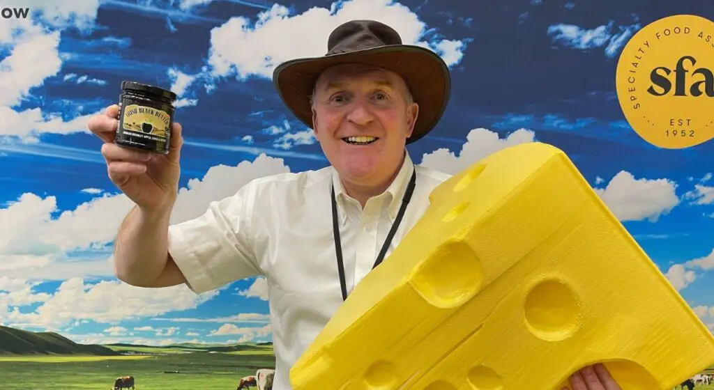 Man holding a large yellow dummy wedge of cheese with holes