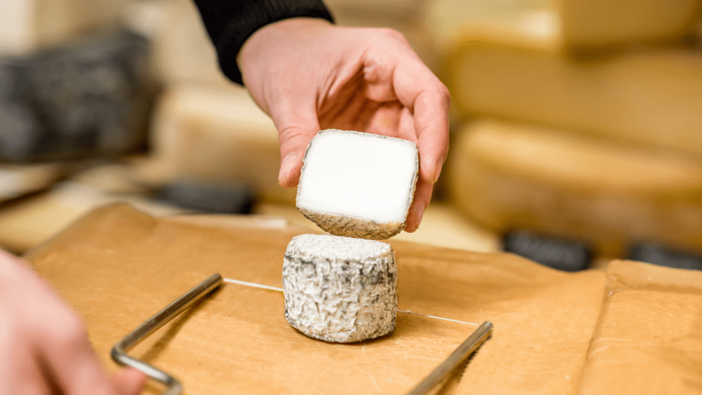 Cheesemonger cutting goats cheese with a small cheese lyre or bow